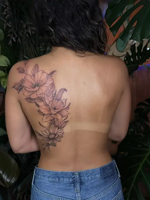 Poppies, daffodils, and a daisy running over the shoulder blade, in fine line.