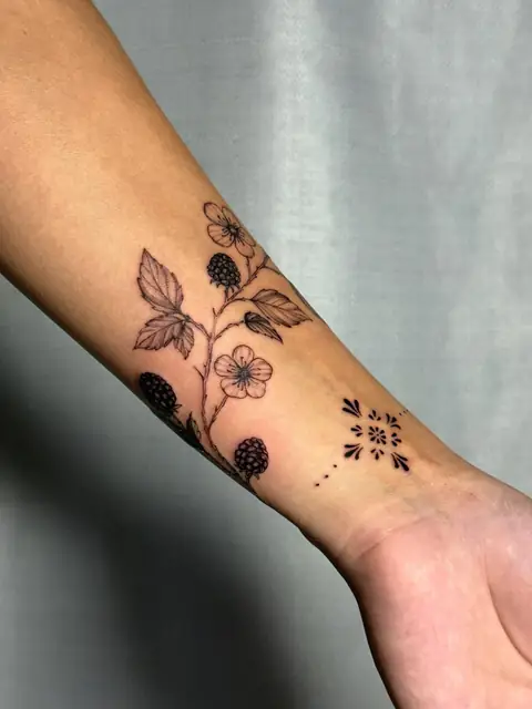 Wild blackberries and blossoms on the forearm, with a small stamp at the wrist.