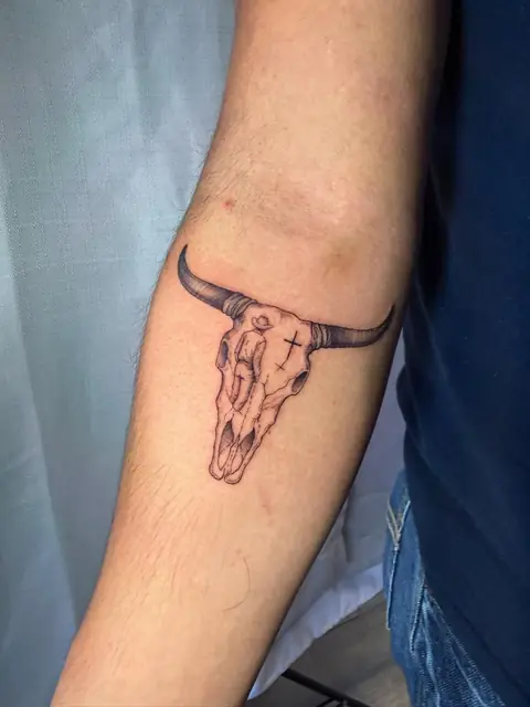 A bull skull with a small cowboy and a cross, on the inner arm.
