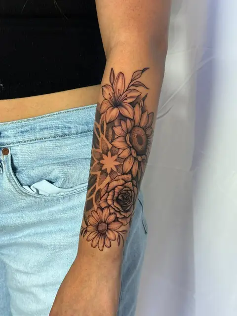 A floral half-sleeve — lily, sunflower, rose, and daisy, with soft shading.