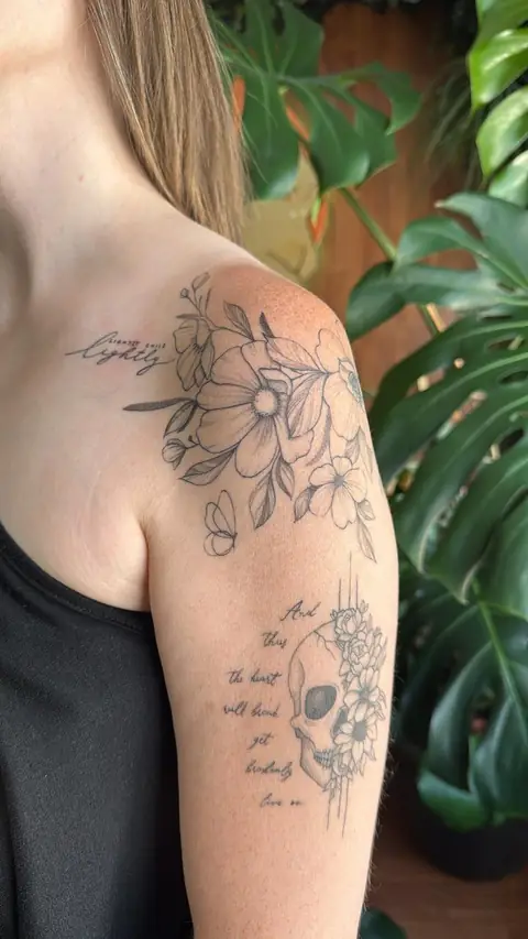 Flowers on the shoulder, a butterfly, and a floral skull with lettering down the arm.