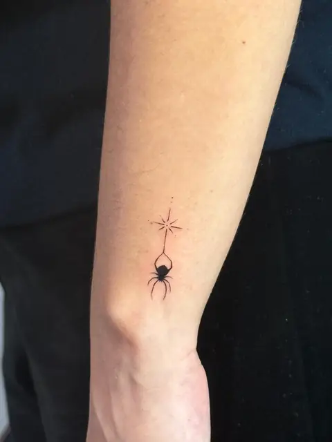 A tiny spider hanging from a star, on the wrist.