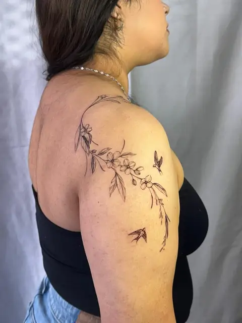 A vine of small blossoms over the shoulder, with two swallows.
